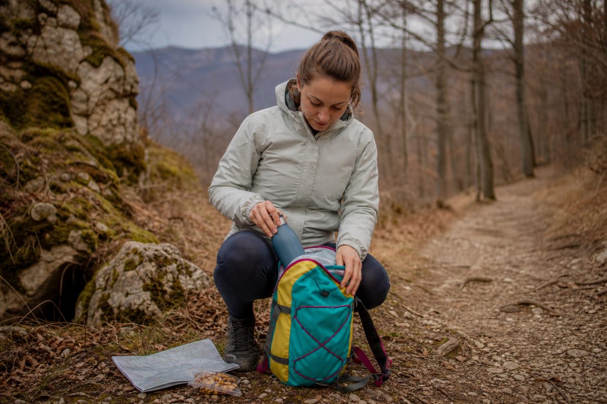 Túrázó színes cotopaxi jellegű hátizsákba pakol erdei ösvény mellett