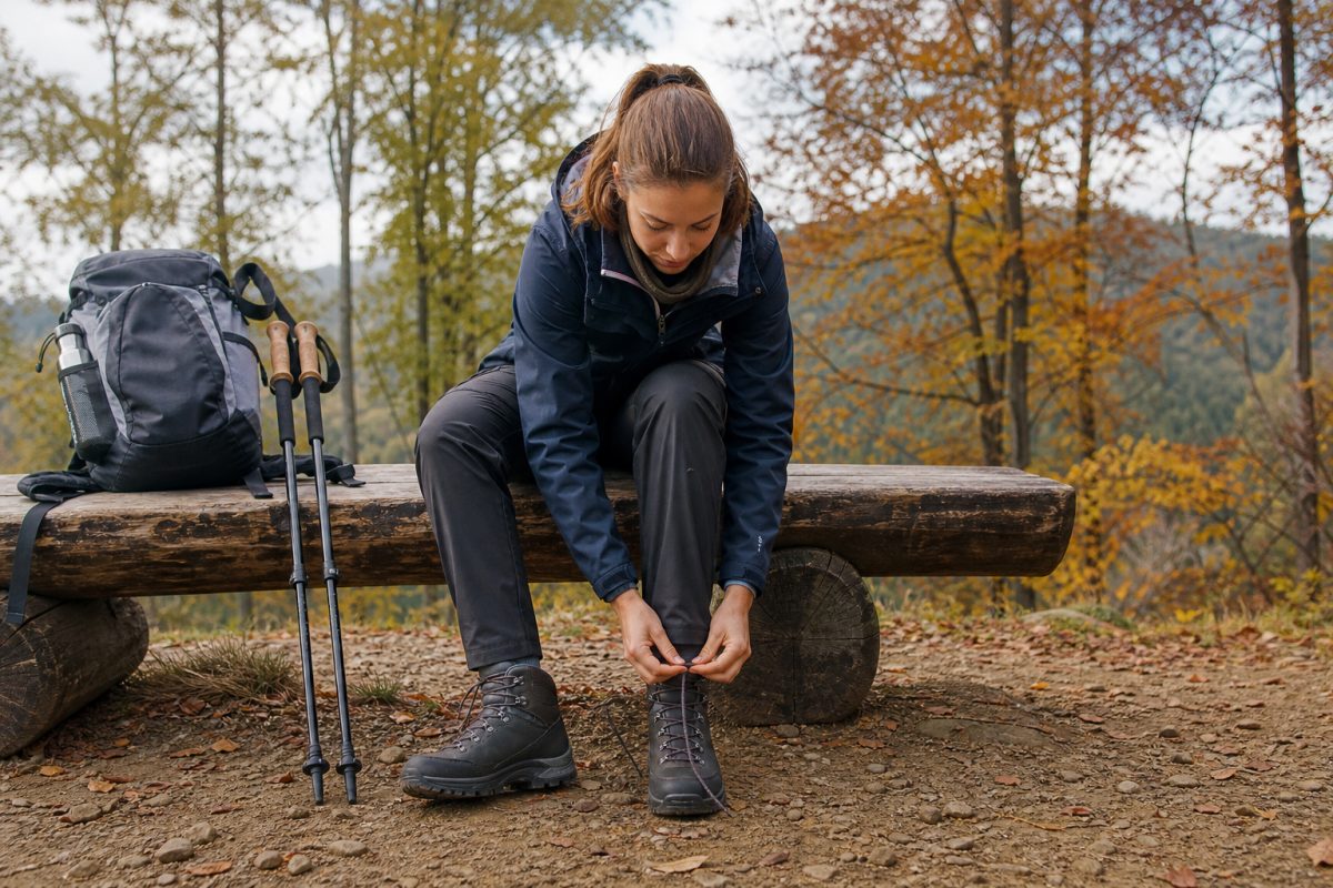 Túrázó középmagas lowa renegade jellegű bakancsot fűz erdei indulás előtt